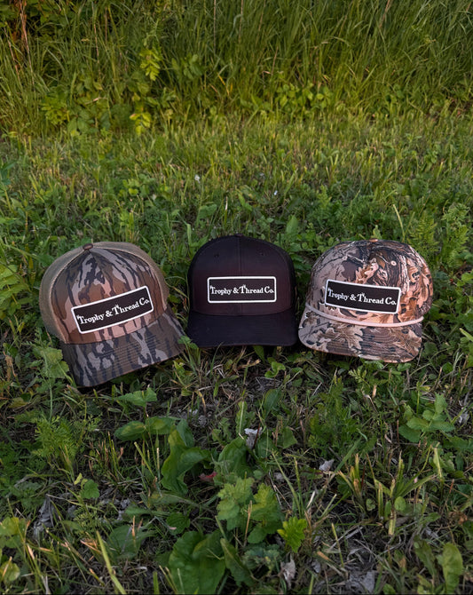 Three caps with 'Trophy & Thorne Co.' logo on grass